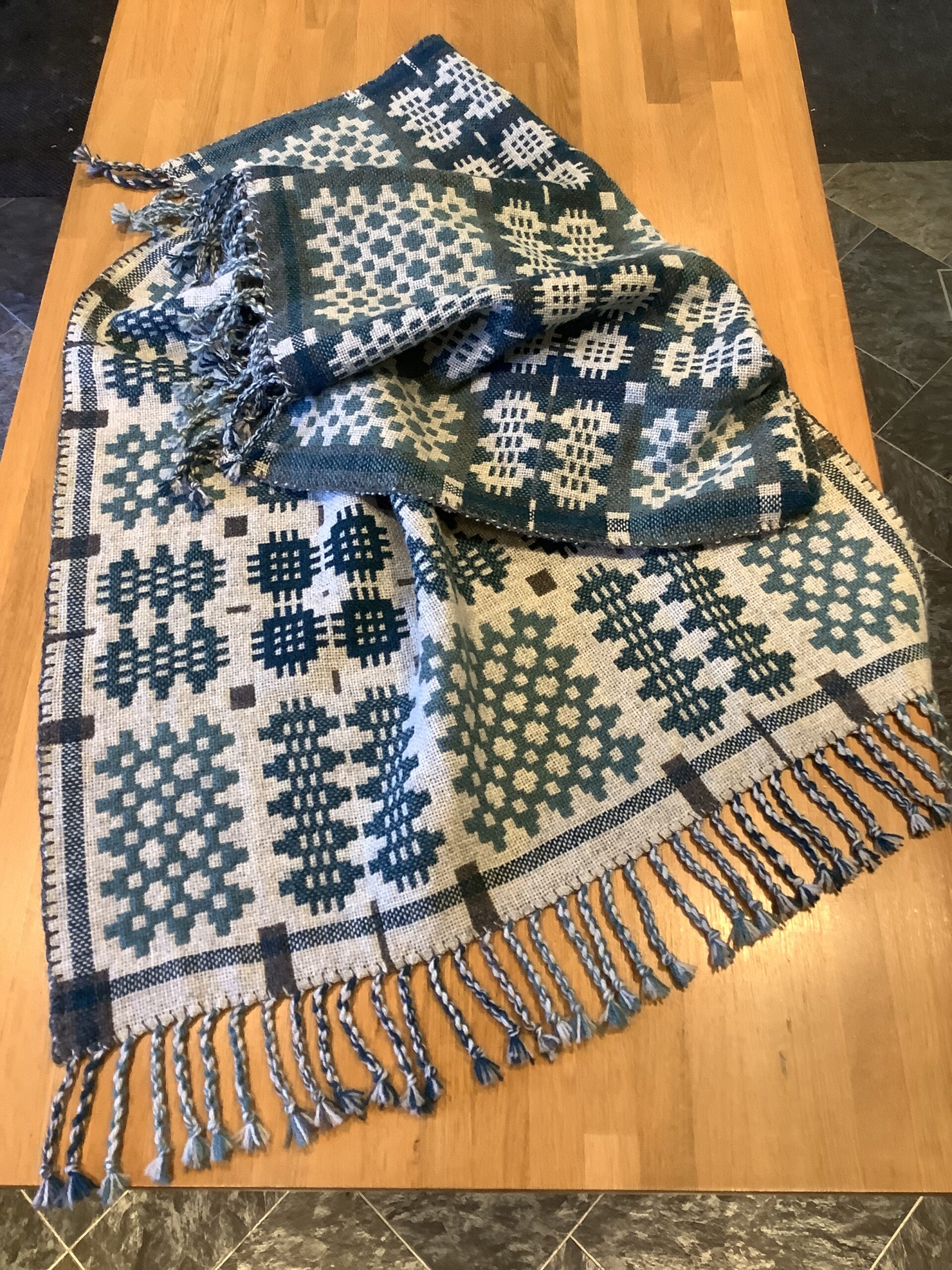 The finished blanket laid on a table. The warp ends have been tied into tassels.