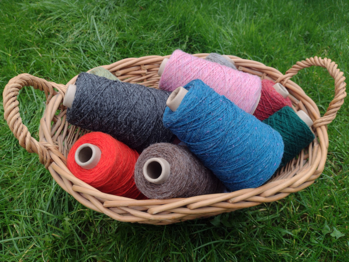 A basket of New Lanark wool in a variety of colours wound onto cones.