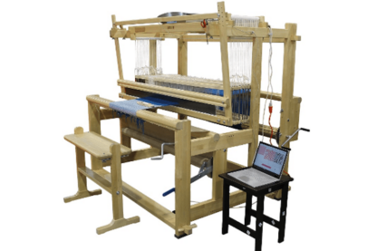 A Toika Eeva loom, made of wood, with a bench and a computer on a low table alongside.